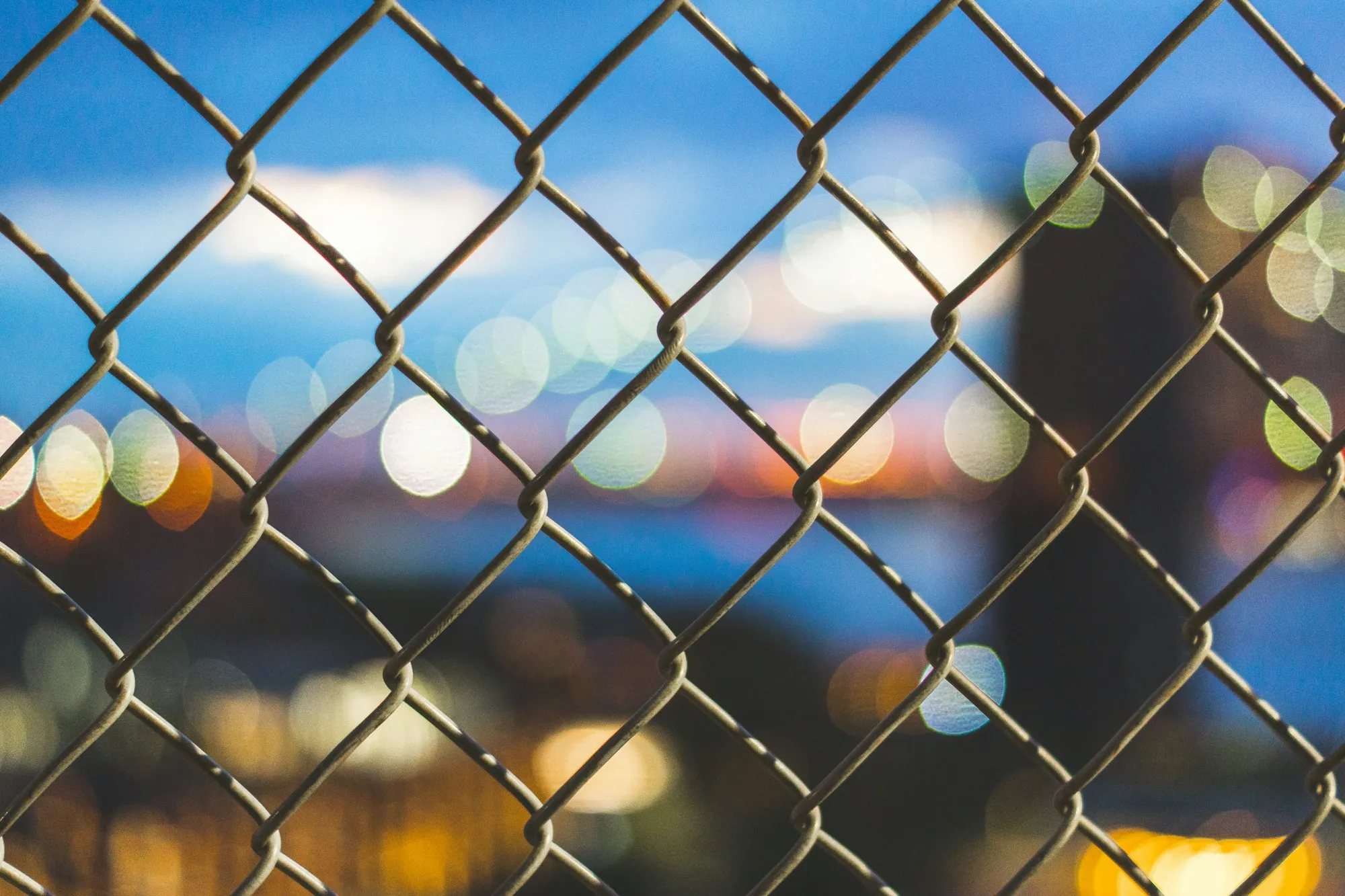 Chain link mesh in close-up with blurred city lights behind it