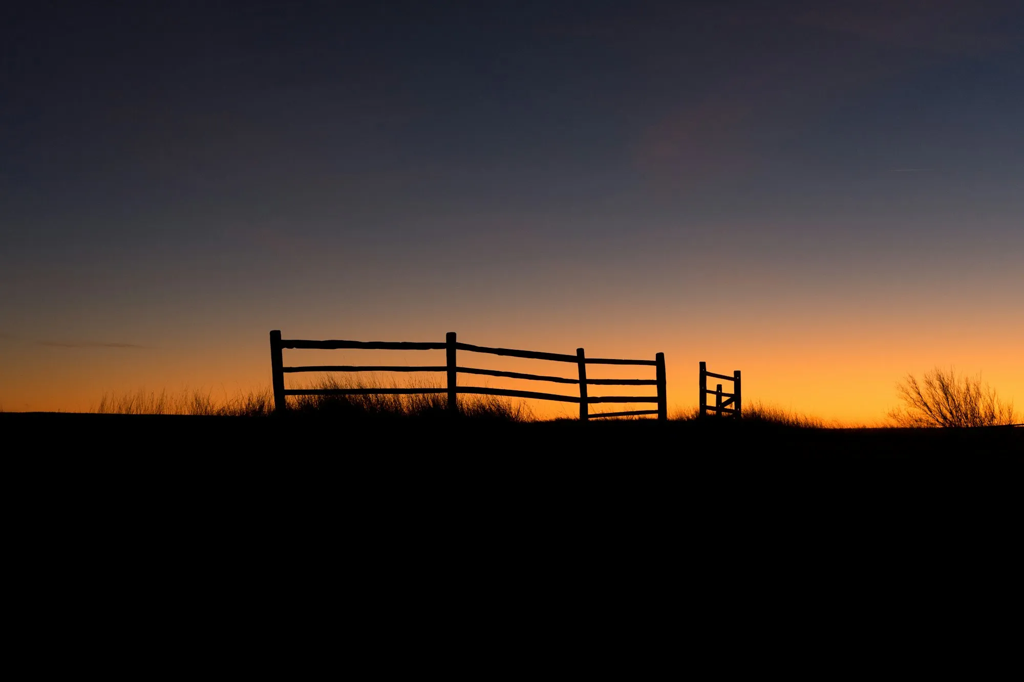 Silhouette of a rail fence and gate against an orange sunset