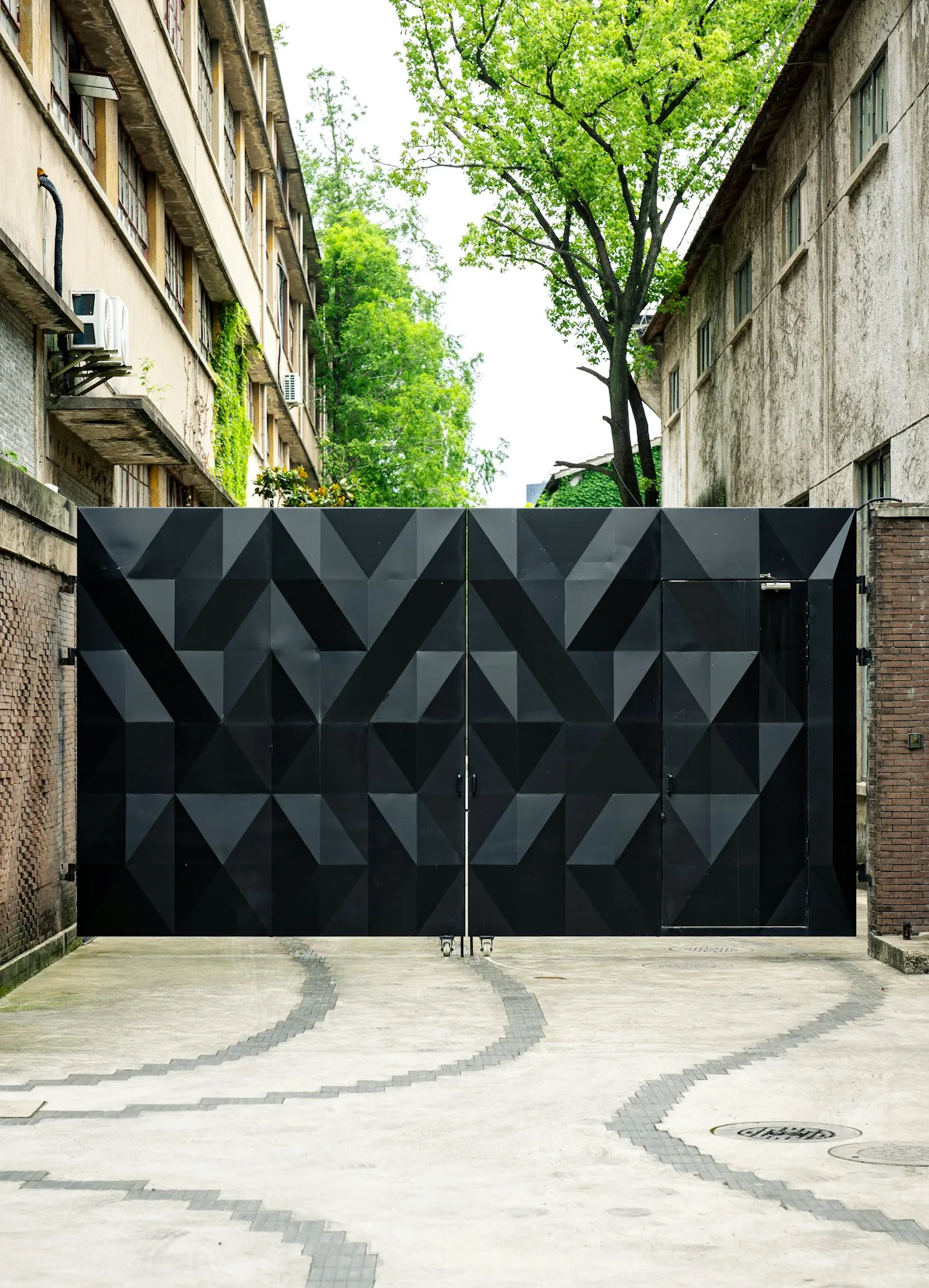 Tall black metal double gate closing a paved driveway between two buildings