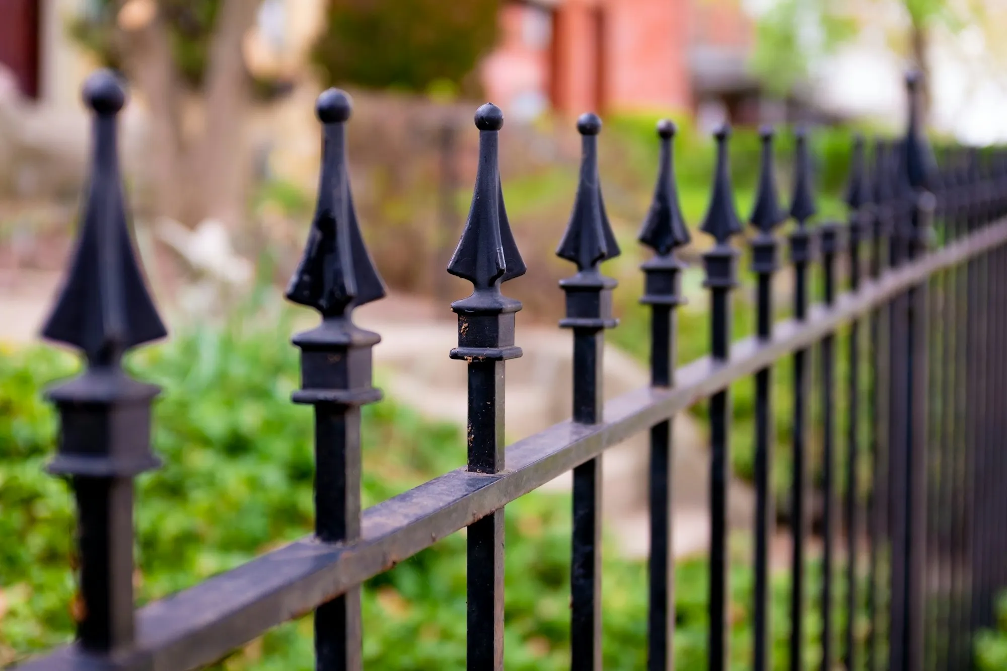 Black ornamental metal fence with spear-point pickets in front of a garden