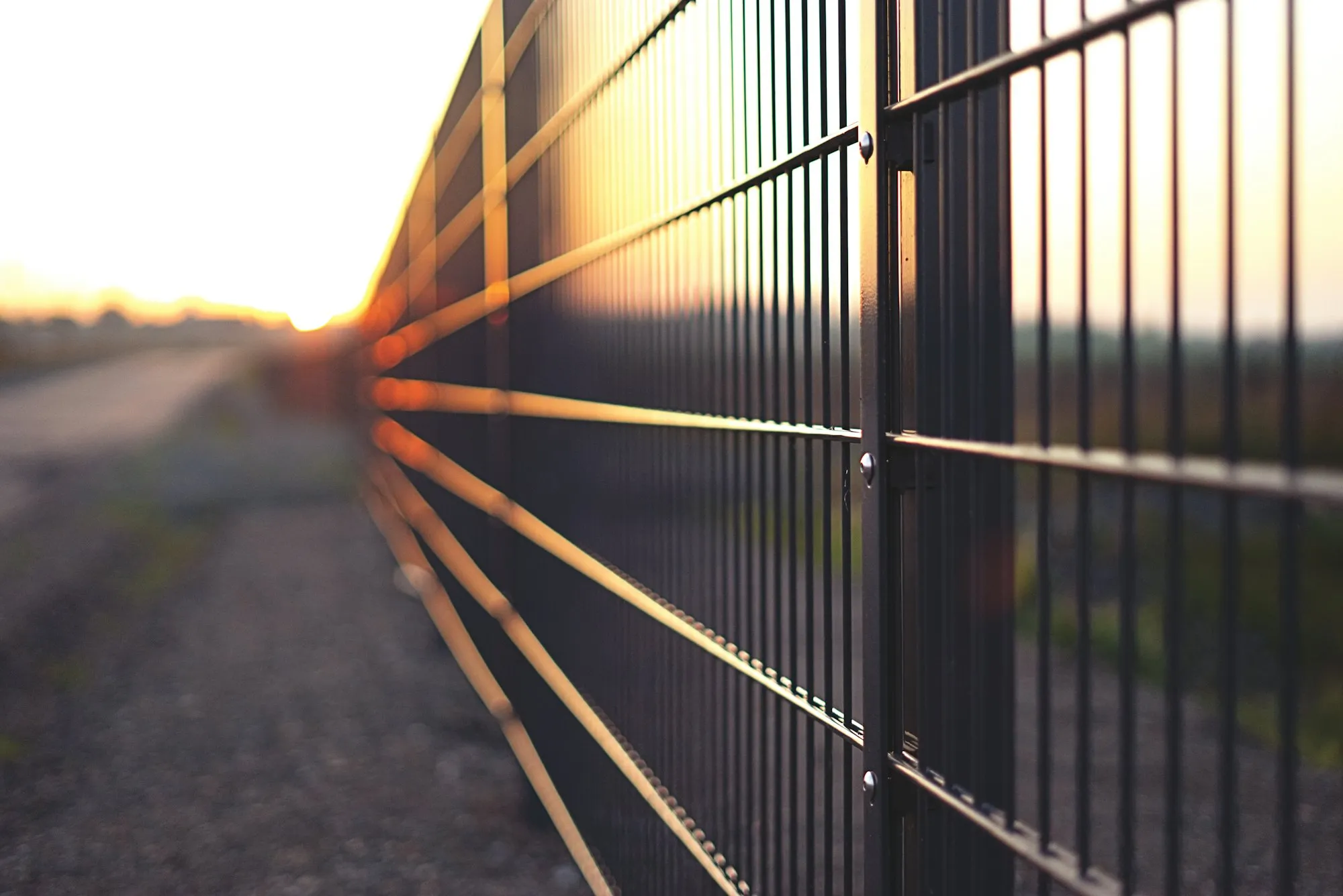 Black welded wire panel fence running along a path at sunset