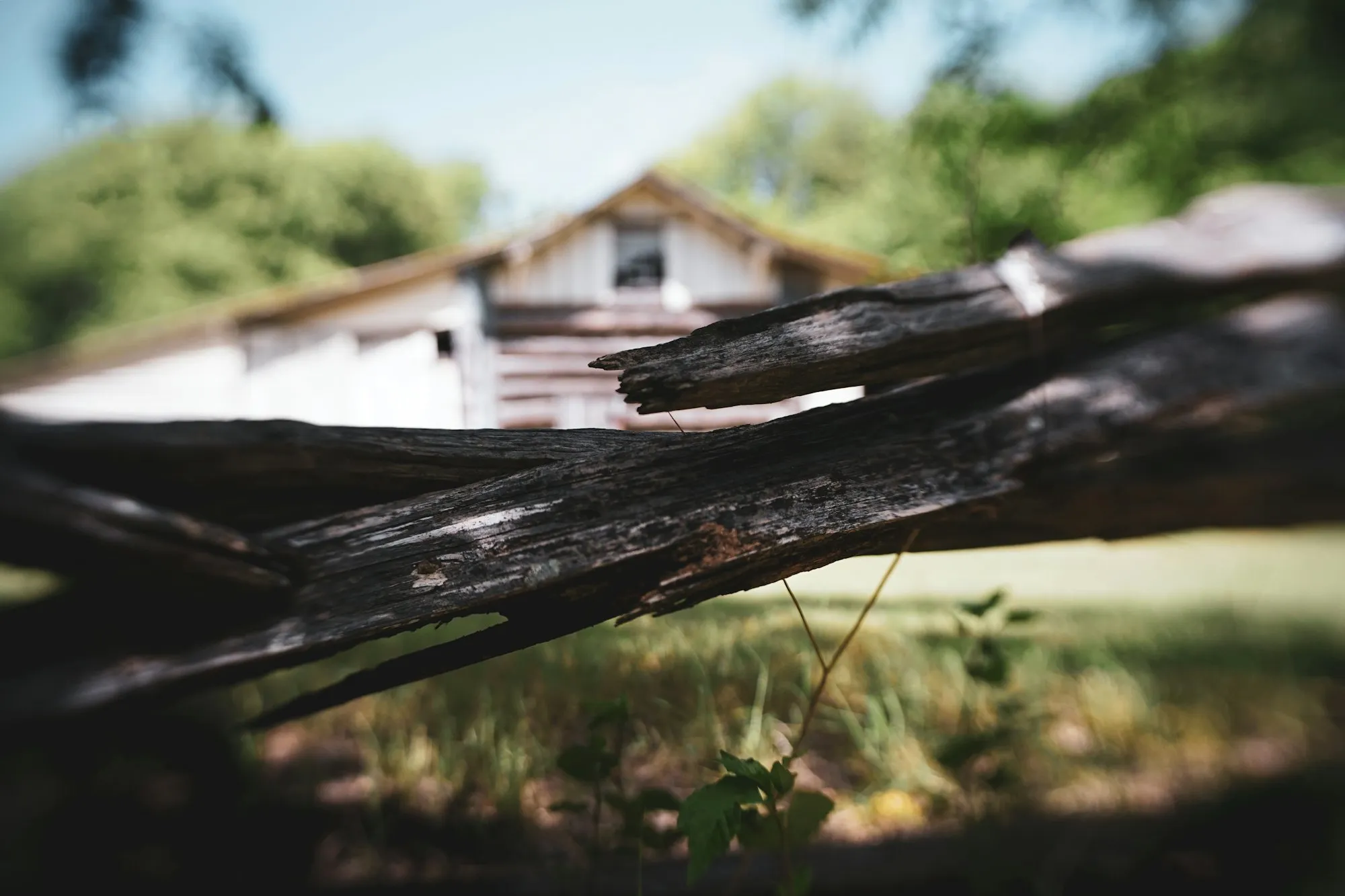 Split, weathered wooden fence rail with an old barn out of focus behind it