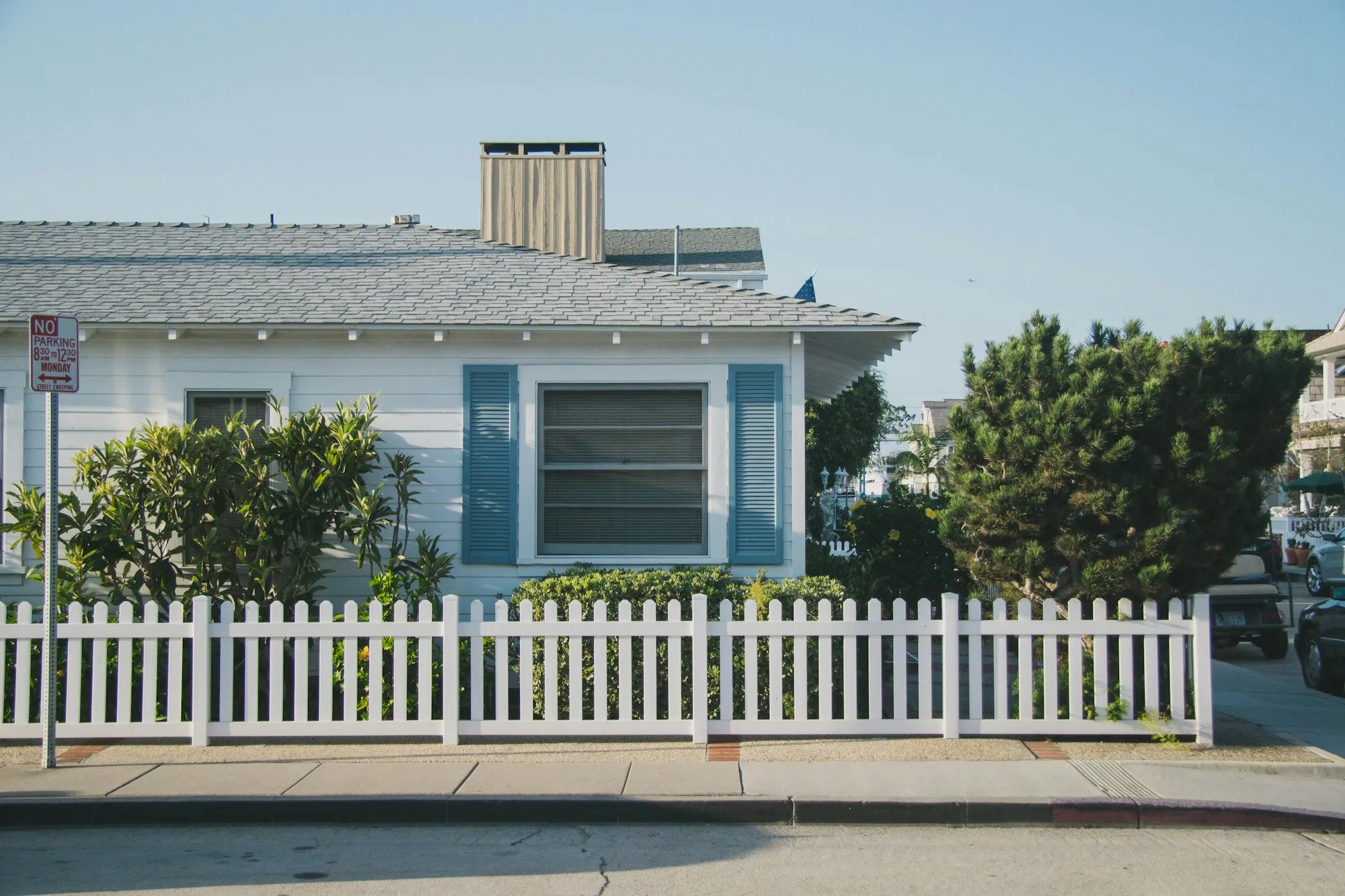 White picket fence along the sidewalk in front of a white house with blue shutters