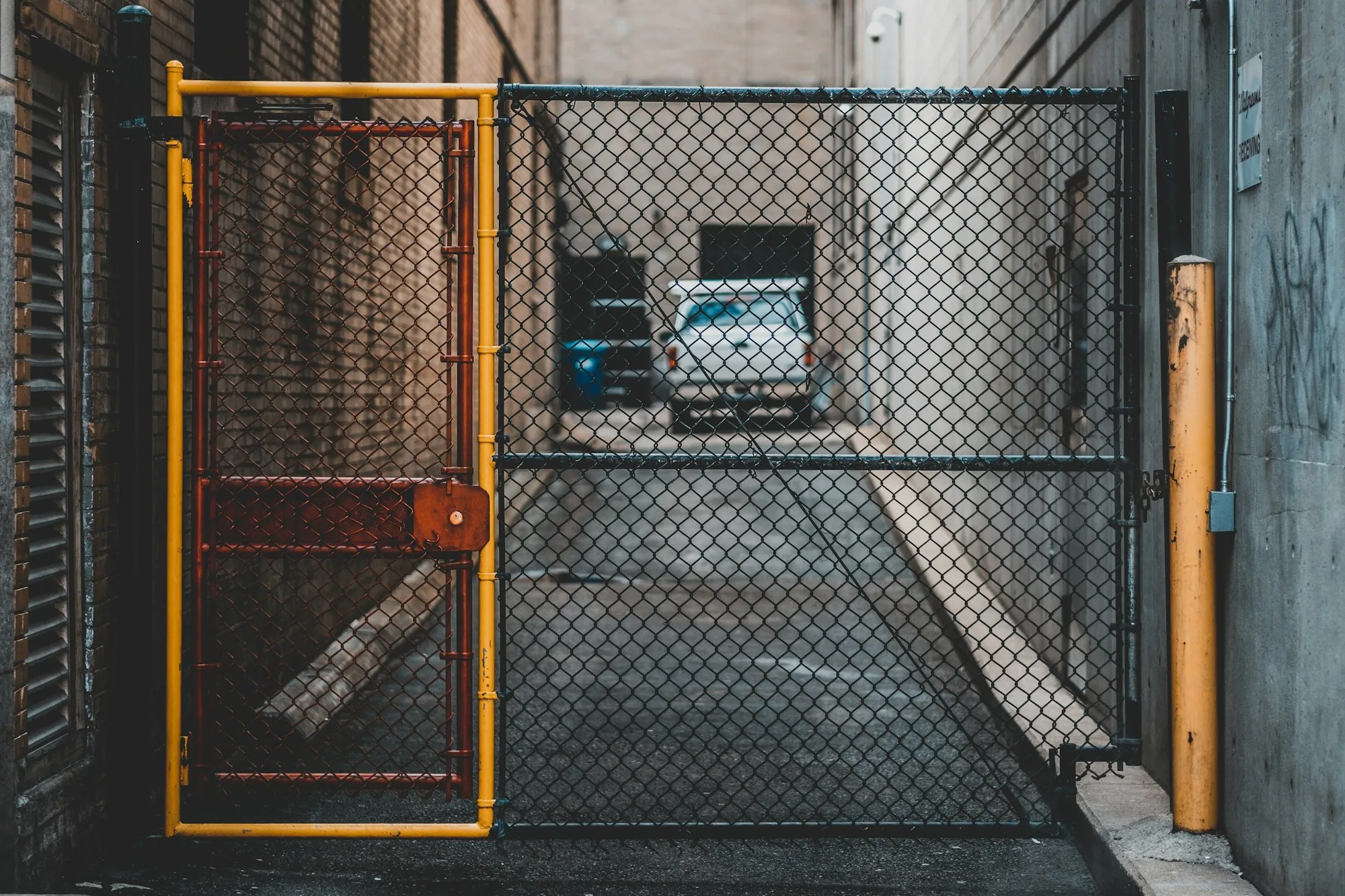 Chain link gate with a yellow frame closing an alley, a pickup truck parked beyond it