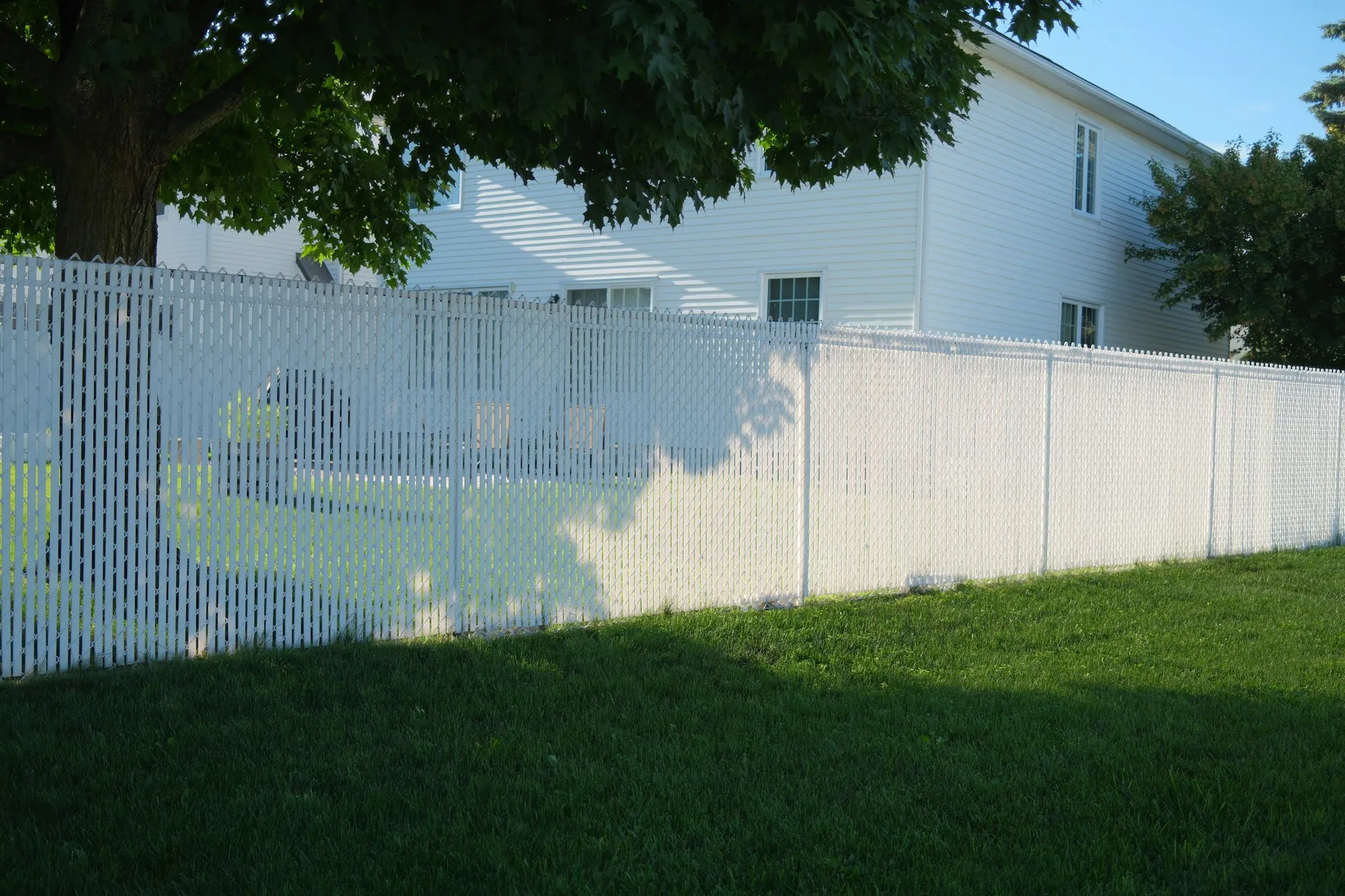 White slatted privacy fence along a shaded lawn beside a white house