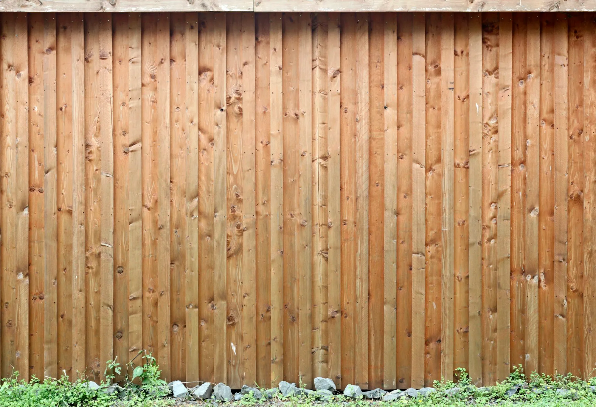 Solid wood board privacy fence with stones and small plants along its base