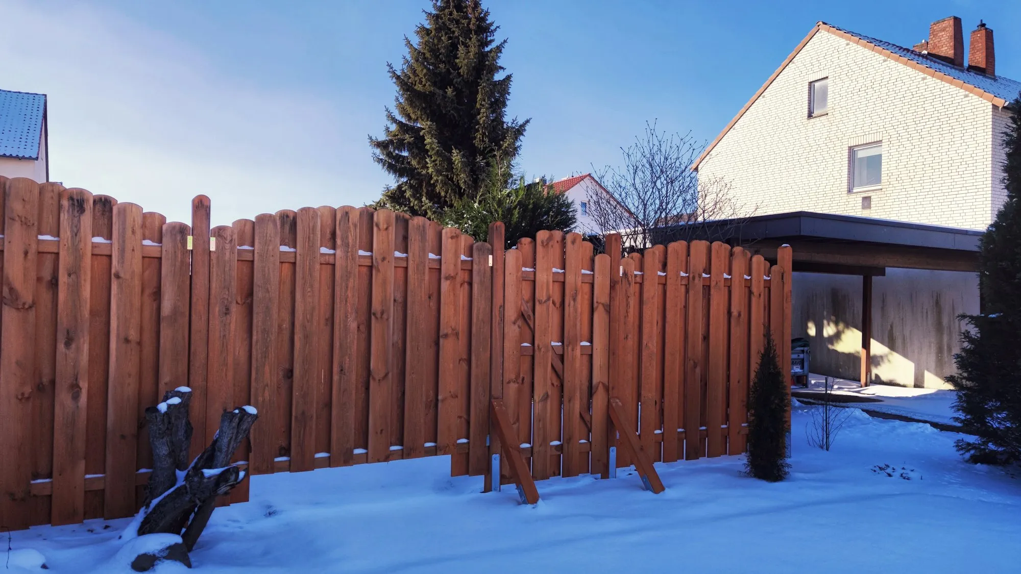 Red-brown wood privacy fence around a snow-covered yard, with houses behind